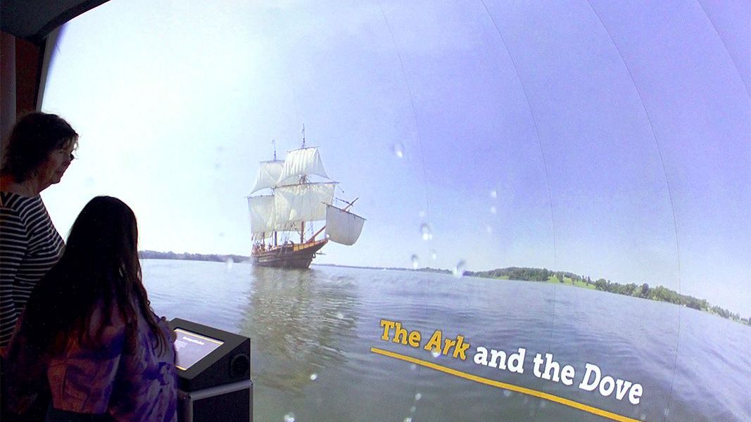 A group of people looking at a ship from in the exhibit while touching the kiosk.