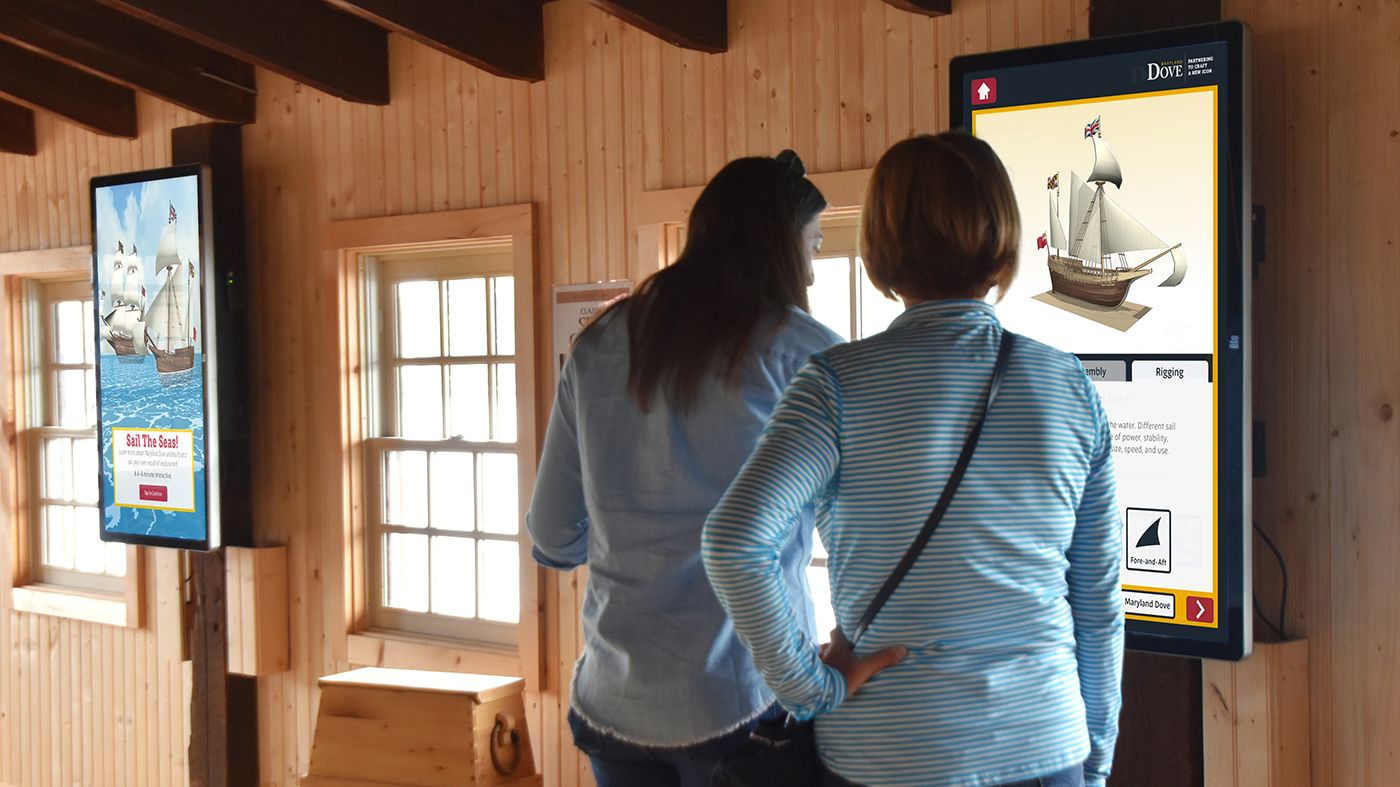 Two women looking at the interactive on a large wall tablet