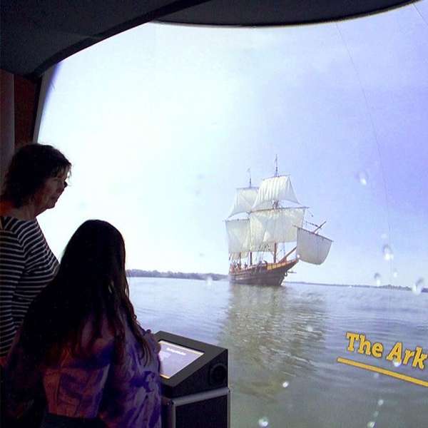 A group of people looking at a ship from in the exhibit while touching the kiosk.