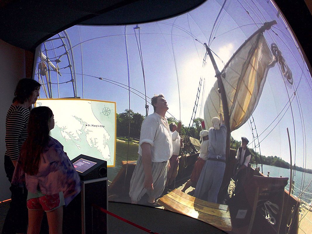 A group of people looking at a ship from in the exhibit while touching the kiosk.